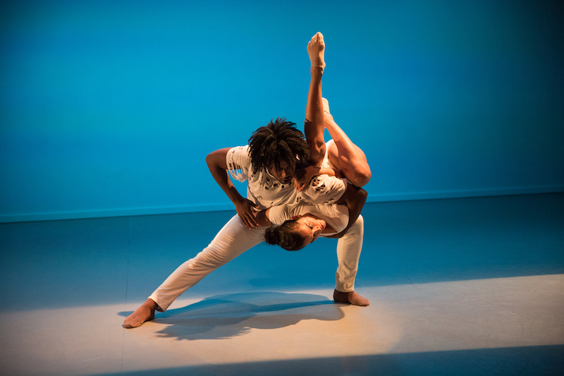 Nigel Campbell rests Kassandra Cruz on his thigh as he's in a lunge. Her head and back rest on his thigh while her legs reach into the air.